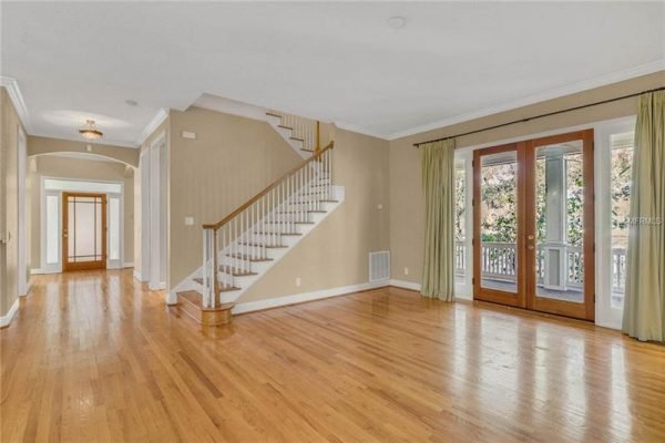 Spacious interior of a Delaney Park home featuring hardwood floors, a staircase, and oversized glass French doors leading to a porch, highlighting the home's modern design and proximity to outdoor living spaces.