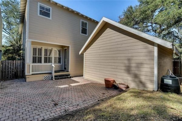 Backyard view of 1125 Delaney Ave, Orlando, FL, featuring a brick patio, detached garage, and fenced yard, highlighting the home's outdoor space near Delaney Park.