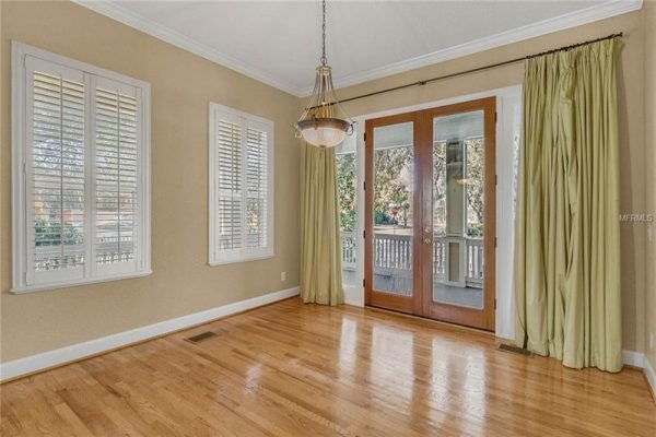 Bright dining area with hardwood floors, large windows featuring plantation shutters, and double glass doors leading to a wrap-around porch, emphasizing indoor-outdoor living in a Delaney Park home.
