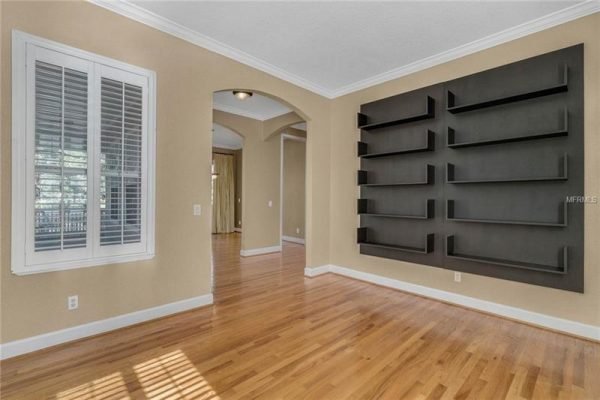 Interior view of a living space featuring hardwood floors, a large wall-mounted bookshelf, and plantation shutters on the windows, showcasing the modern design of the home at 1125 Delaney Ave, Orlando, FL.
