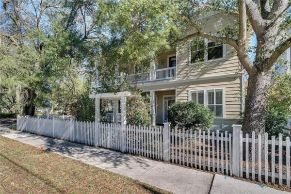 Charming two-story home at 1125 Delaney Ave, Orlando, FL, featuring a white picket fence, large corner lot, wrap-around porches, and mature oak trees, ideally located across from Delaney Park.