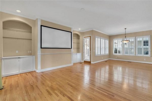 Spacious living area with hardwood floors, built-in cabinetry, and large windows, featuring a wall-mounted screen and access to a patio, ideal for entertaining in a Delaney Park home.