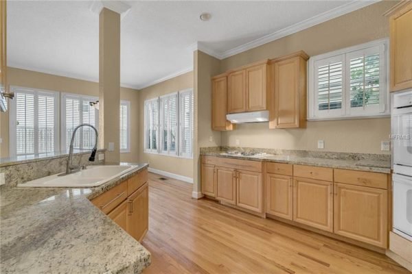 Modern kitchen with granite countertops, light wood cabinetry, and large windows featuring plantation shutters, showcasing a bright and inviting space in a Delaney Park home.
