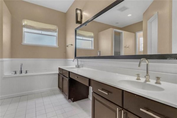 Spacious bathroom featuring dual sinks, dark wood cabinetry, large mirror, and natural light from windows, with a separate shower area and bathtub, reflecting modern design in a Delaney Park home.