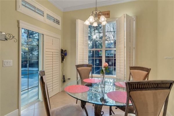 Bright breakfast nook with glass table and pink placemats, featuring a view of the screened pool through large windows, in a Windermere home for sale.