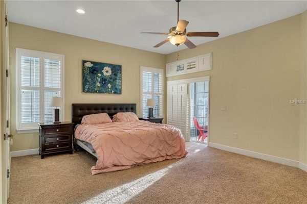 Spacious bedroom in Windermere home featuring a king-size bed with pink bedding, a wooden nightstand, large windows with plantation shutters, and a ceiling fan, showcasing a bright and inviting atmosphere.