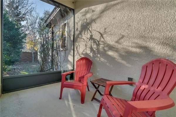 Screened porch featuring two red Adirondack chairs and a small side table, surrounded by greenery and natural light, ideal for relaxation in a Windermere home.