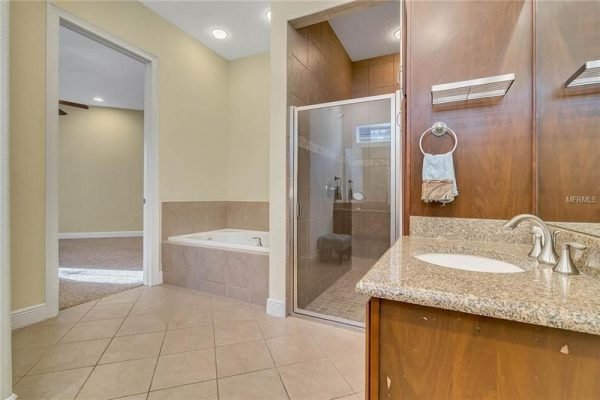 Spacious bathroom featuring a glass shower, soaking tub, dual sinks with granite countertops, and tile flooring, showcasing a modern design in a Windermere home.