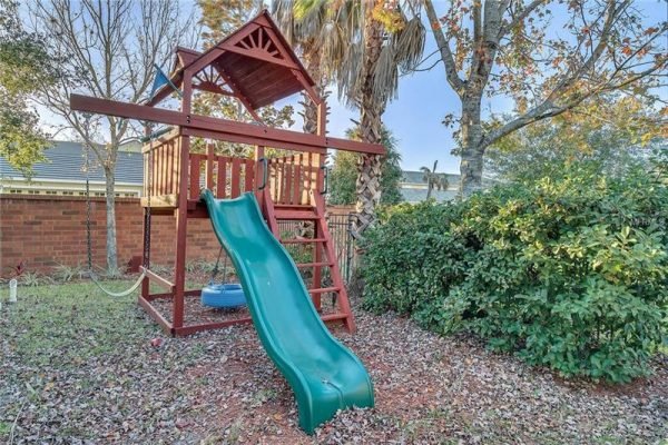Playset with slide in backyard of Windermere home, surrounded by greenery and palm trees, highlighting family-friendly outdoor space.