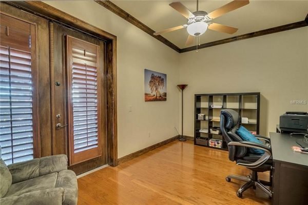 Home office with wood flooring, ceiling fan, and window shutters, featuring a desk and chair, showcasing a cozy workspace in a Windermere property.