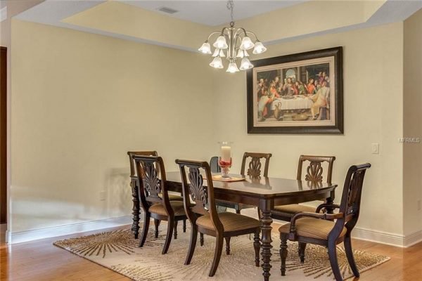 Dining area featuring a wooden table with six chairs, decorative chandelier, and a large painting on the wall, showcasing an elegant interior design in a Windermere home.