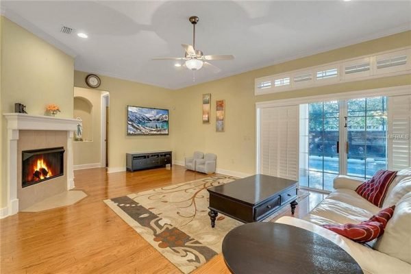 Living room with hardwood floors, fireplace, and large windows showcasing the screened pool area, featuring a TV mounted on the wall and comfortable seating, ideal for showcasing the Windermere home's spacious and inviting interior.