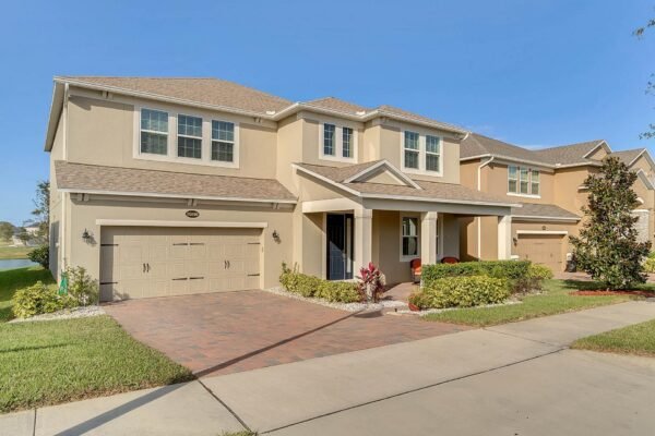Front view of 15890 Citrus Grove Loop, a spacious residential home in Winter Garden, FL, featuring a well-maintained facade, two-car garage, landscaped yard, and proximity to a pond, showcasing the property’s inviting curb appeal.