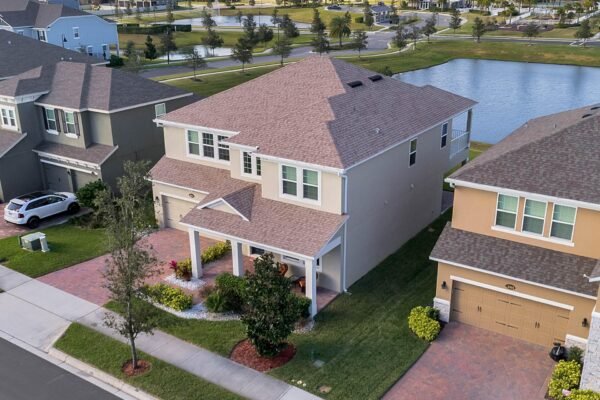 Aerial view of a modern two-story home at 15890 Citrus Grove Loop, Winter Garden, FL, featuring a landscaped front yard, driveway, and proximity to a serene pond, highlighting the premium lot with no rear neighbors.