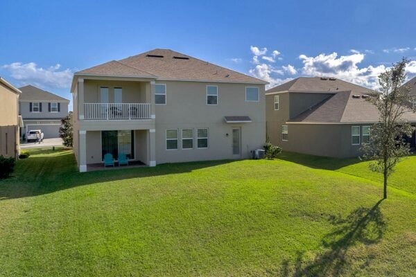 Aerial view of a modern two-story home at 15890 Citrus Grove Loop, Winter Garden, FL, featuring a spacious backyard, balcony, and no rear neighbors, surrounded by well-maintained lawns and neighboring houses.