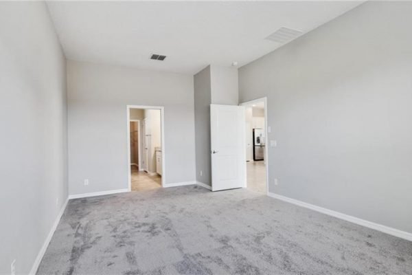 Spacious, light-filled interior of a new home at 2192 Antilles Club Dr, Kissimmee, FL, featuring plush carpet, neutral walls, and doorways leading to kitchen and bathroom, ideal for 55+ community living.