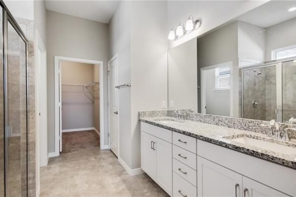 Modern bathroom interior with double sink vanity, granite countertop, and spacious layout featuring a walk-in closet and glass shower, showcasing the design of a 55+ community home in Kissimmee, FL.