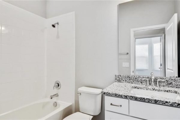 Bathroom featuring a bathtub, toilet, and granite countertop with dual sinks, showcasing modern design elements in a newly constructed home at 2192 Antilles Club Dr, Kissimmee, FL.