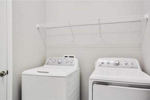 Laundry room featuring a white washing machine and dryer, with a shelf above for storage, showcasing a clean and functional design ideal for a new home in a 55+ community.