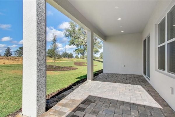 Covered patio area with paver flooring overlooking landscaped green space in a new home at Four Seasons, Kissimmee, FL, designed for the 55+ community.
