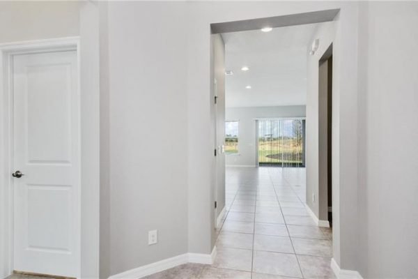Interior view of 2192 Antilles Club Dr, Kissimmee, FL, featuring a hallway with tile flooring, light gray walls, and doorways leading to living spaces, highlighting the modern design of a new home in a 55+ community.