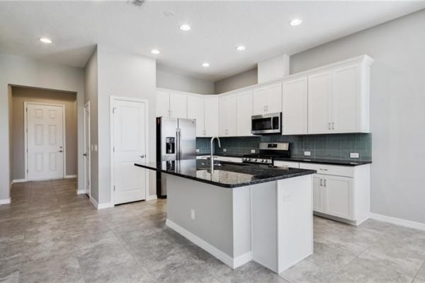 Modern kitchen interior featuring granite countertops, stainless steel appliances, and white cabinetry in a new home at 2192 Antilles Club Dr, Kissimmee, FL, highlighting amenities for a 55+ community lifestyle.