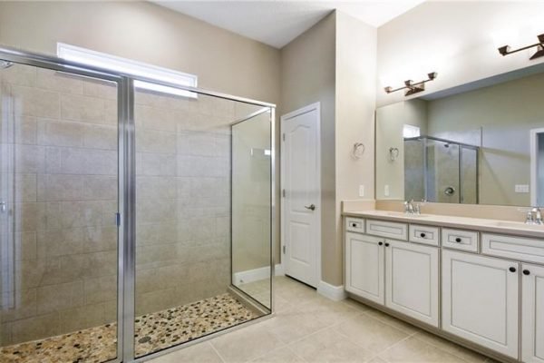 Spacious bathroom featuring a glass-enclosed shower, dual sink vanity with white cabinetry, and neutral tile flooring, highlighting modern design in a new home at Four Seasons, Kissimmee, FL.