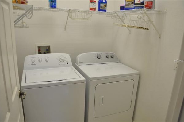 Laundry room featuring a Whirlpool washing machine and dryer, with shelving above for storage, in a residential setting at 117 Crepe Myrtle Dr, Groveland, FL.