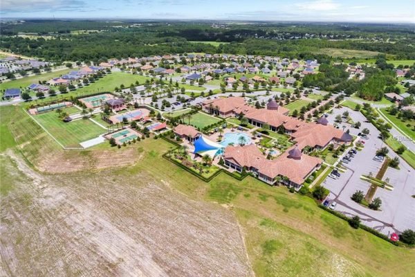 Aerial view of Trilogy, a luxurious over 55 community in Groveland, FL, showcasing resort-style amenities including a swimming pool, tennis courts, and landscaped grounds, surrounded by residential homes.