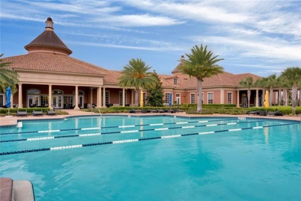 Resort-style swimming pool with lap lanes, surrounded by palm trees and a luxurious clubhouse in Trilogy, Groveland, FL.