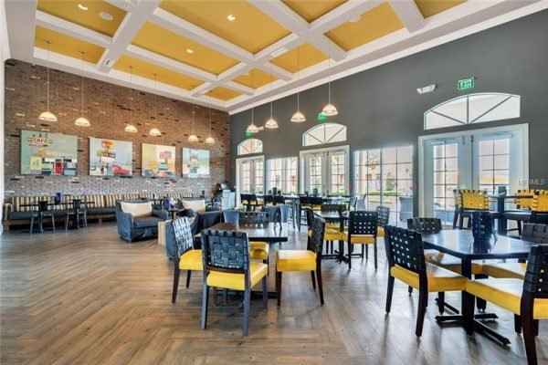 Interior view of a modern dining area in Trilogy, Groveland, FL, featuring yellow and black chairs, wooden flooring, large windows, and a brick accent wall with artwork.