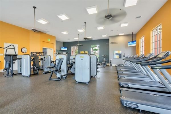 Gym interior featuring modern fitness equipment, treadmills, and exercise machines in a bright, well-lit space with orange and gray walls, ideal for residents of Trilogy's 55+ community in Groveland, FL.
