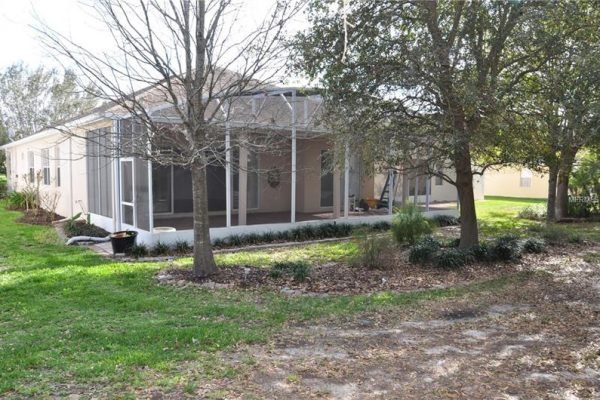 Exterior view of a single-family home in Groveland, FL, featuring a screened-in patio, landscaped yard with trees, and no rear neighbors, highlighting the tranquil living environment in the Trilogy over 55 community.