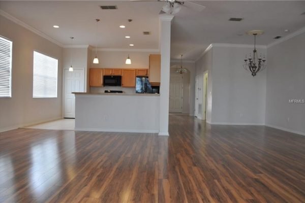 Spacious open floor plan of a modern living area featuring hardwood floors, kitchen with dark appliances, and natural light from large windows, highlighting the inviting ambiance of the home at 117 Crepe Myrtle Dr, Groveland, FL.