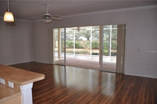 Open living area with new PERGO flooring, ceiling fan, and sliding glass doors leading to a covered lanai in a Groveland, FL home for sale in the Trilogy community.