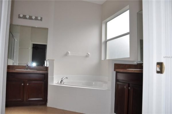 Bright and spacious bathroom featuring dual vanities, a large soaking tub, and natural light from windows, showcasing the upscale amenities of the Groveland, FL home at 117 Crepe Myrtle Dr.