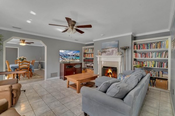 Living room in Windermere home featuring gray walls, tile flooring, blue sofa, wooden coffee table, fireplace with TV above, and bookshelves filled with books.