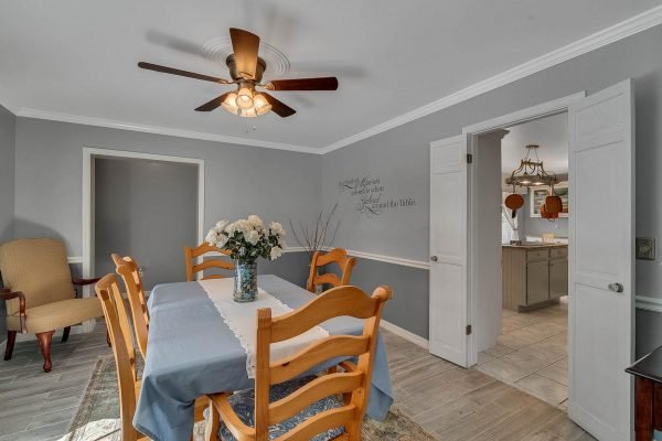 Dining room with wooden table and chairs, decorative centerpiece, ceiling fan, and doorway leading to kitchen, showcasing modern interior design in Windermere, FL home.