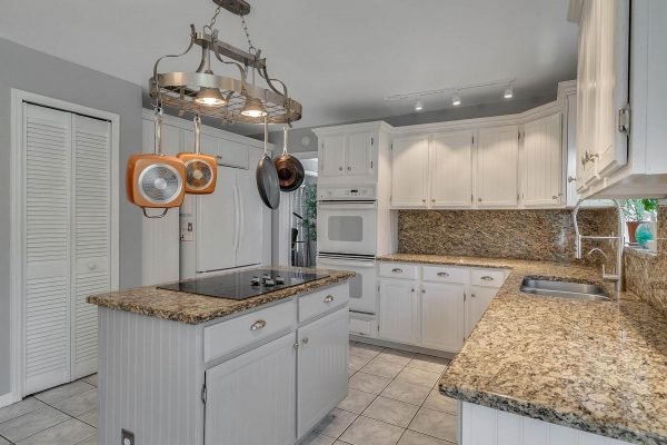 Kitchen featuring white cabinetry, granite countertops, stainless steel appliances, and a kitchen island with a modern hanging light fixture, set in a spacious layout.
