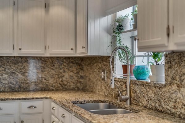 Modern kitchen with granite countertops, double sinks, and white cabinetry, featuring plants in windowsill.