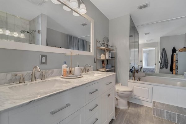 Modern master bathroom featuring dual sinks with marble countertop, stylish fixtures, and a large mirror, complemented by a neutral color palette and contemporary decor.