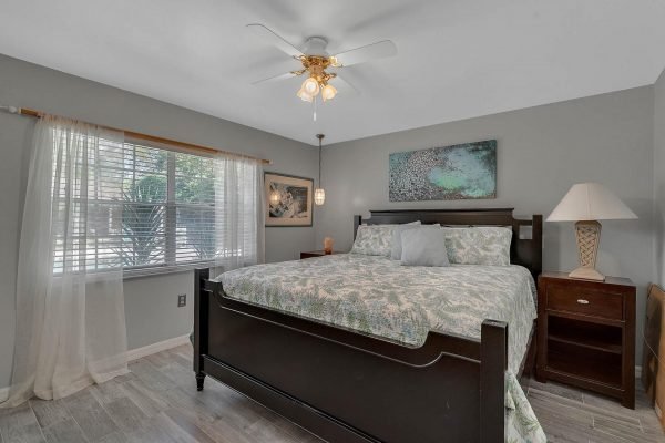 Cozy bedroom featuring a queen-sized bed with decorative bedding, window with sheer curtains allowing natural light, wooden nightstand with lamp, and artwork on the wall, in a Windermere estate.
