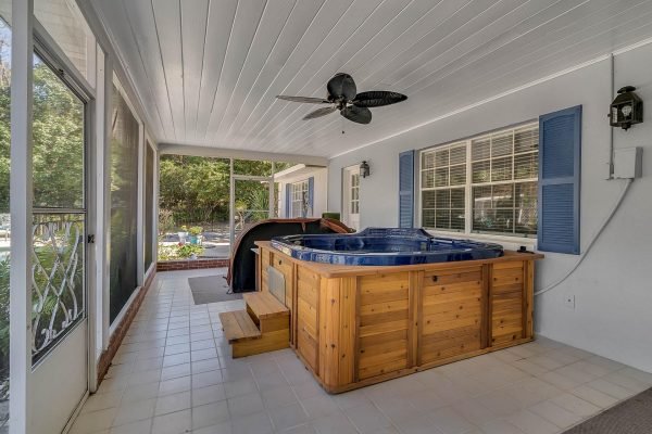Covered lanai with a wooden hot tub, ceiling fan, and large windows overlooking the backyard in a Windermere, FL estate, featuring a spacious layout and outdoor entertaining area.
