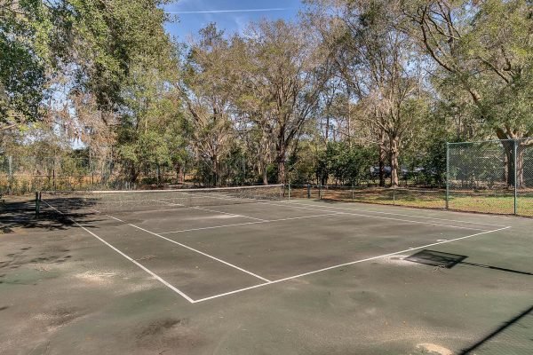 Private tennis court surrounded by mature trees in Windermere, Florida, showcasing outdoor recreational space for the estate at 1421 Crescent Lake Dr.