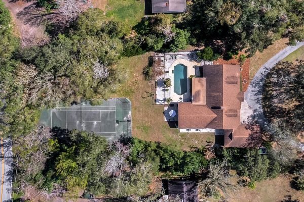 Aerial view of 1421 Crescent Lake Dr in Windermere, FL, featuring a spacious one-story estate with a large pool, extensive decking, and a private tennis court surrounded by lush greenery.