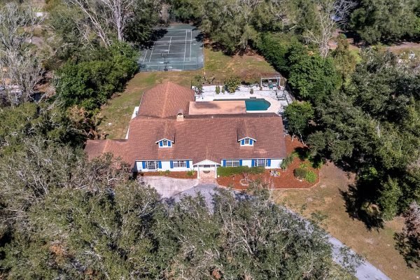 Aerial view of 1421 Crescent Lake Dr, Windermere, FL, showcasing a spacious one-story estate with a large pool, private tennis court, and surrounding mature trees.