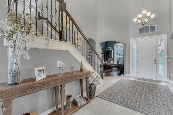 Welcoming entryway of 15455 Sandfield Loop, Winter Garden, featuring elegant staircase, decorative console table, and large windows providing natural light, showcasing the home's open floor plan.