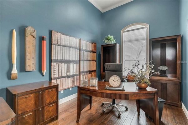 Elegant home office featuring a modern desk, wooden cabinetry, decorative wall art, and large windows providing natural light, located in the Abbott floor plan at 15455 Sandfield Loop, Winter Garden, FL.