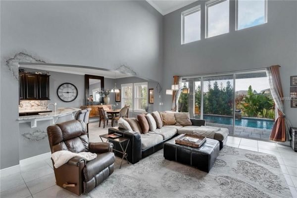 Spacious living room featuring a modern design with a sectional sofa, recliner, and large windows overlooking a backyard pool, part of the Abbott floor plan in Winter Garden, FL.