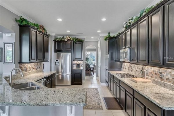 Modern kitchen with dark wood cabinetry, granite countertops, stainless steel appliances, and open layout leading to dining area, showcasing elegance and functionality in a Winter Garden home.